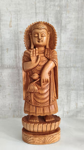 Hand-carved wooden standing Buddha statue with a serene expression, holding his right hand in the Abhaya Mudra (gesture of fearlessness), on a lotus base.